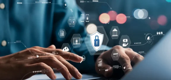 Close-up of hands on a computer keyboard with digitally superimposed icons on IT security, such as a lock, documents, servers and mobile devices - illustrating modern cyber security in everyday business life.