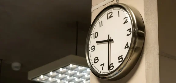 Wall clock with silver frame showing 9 o'clock, taken in an interior with ceiling lighting.