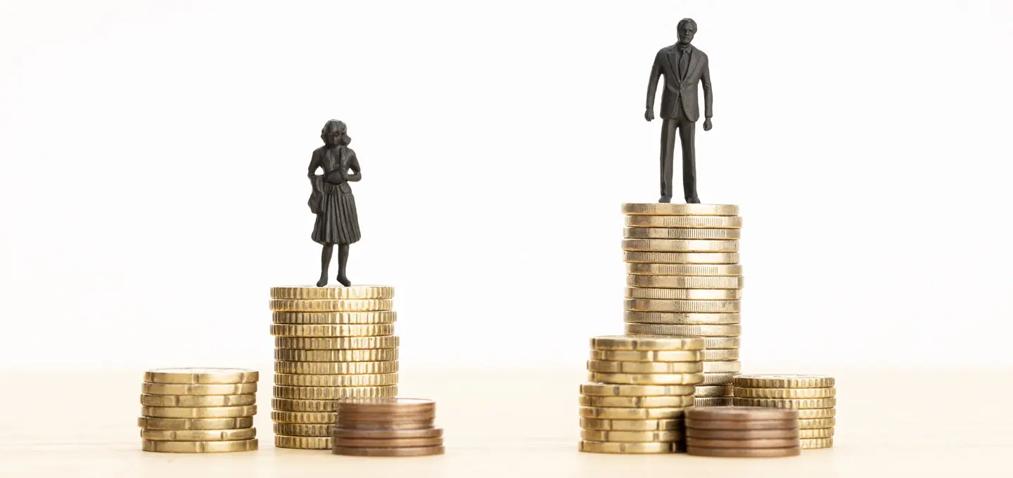 Eine kleine Frauenfigur steht auf einem niedrigeren Stapel Goldmünzen, während eine Männerfigur auf einem deutlich höheren Münzstapel steht. Das Bild verdeutlicht ungleiche Bezahlung zwischen Männern und Frauen.