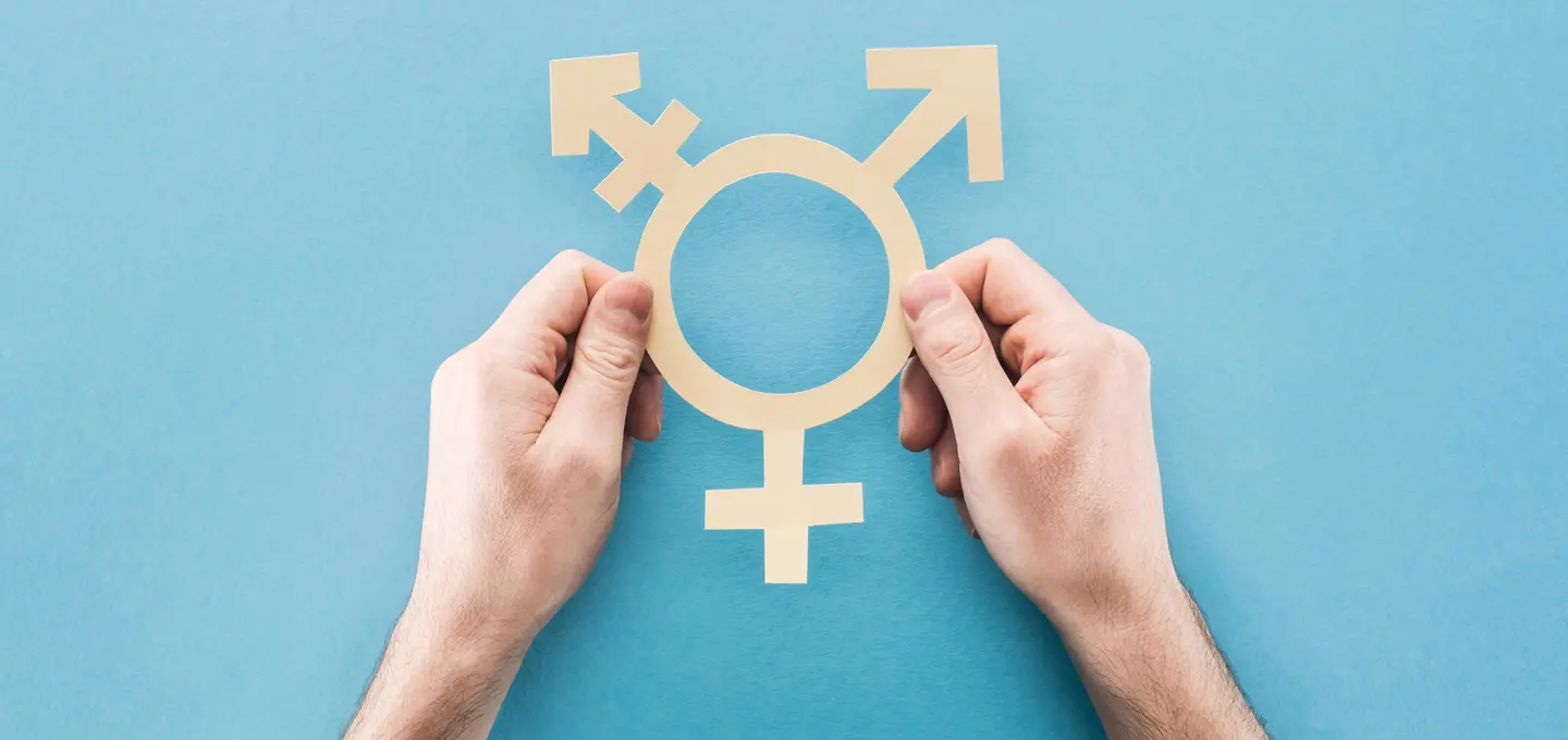 Zwei Hände halten ein ausgeschnittenes Transgender-Symbol auf blauem Hintergrund.