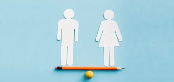 Paper cut-outs of a male and a female figure balancing on a pencil lying on a small yellow ball