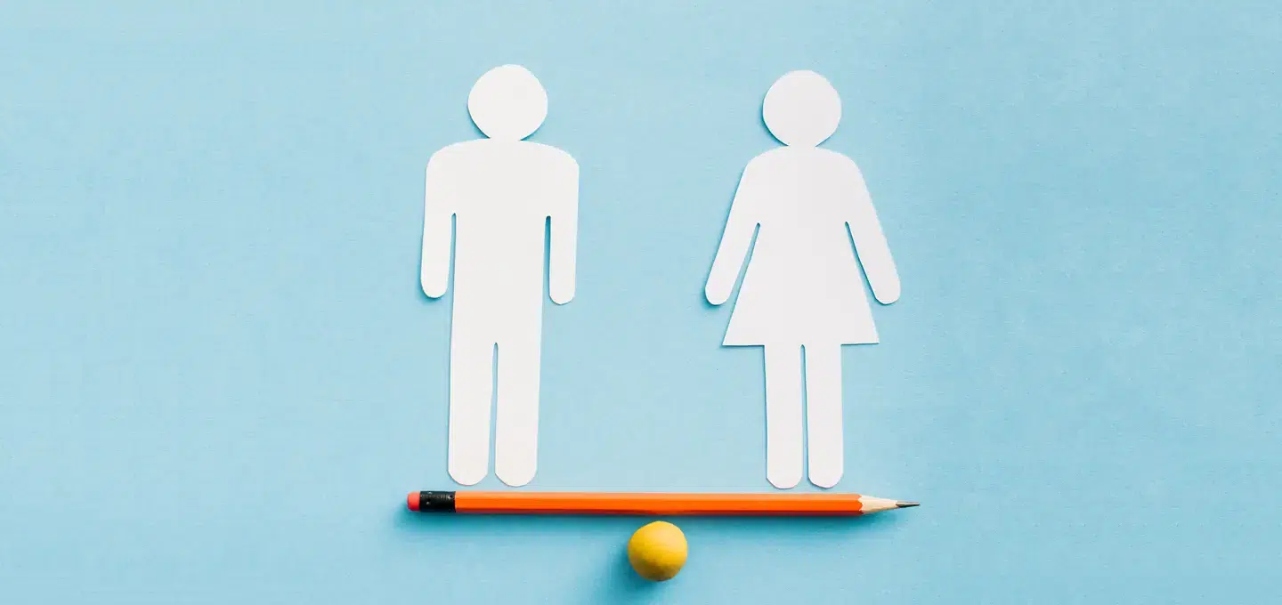 Paper cut-outs of a male and a female figure balancing on a pencil lying on a small yellow ball