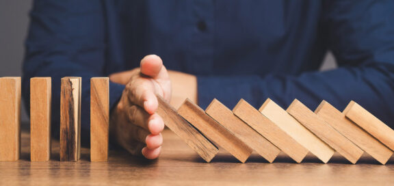Hand stoppt fallende Dominosteine – Symbolbild für Risikomanagement, Krisenprävention und strategische Unternehmenssicherheit