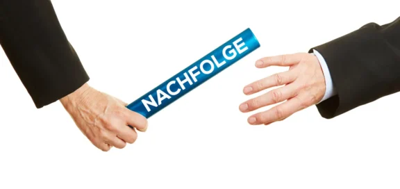 Zwei Geschäftspersonen in Anzügen übergeben einen Staffelstab mit der Aufschrift ‚Nachfolge‘ – ein Sinnbild für die Unternehmensnachfolge an die nächste Generation