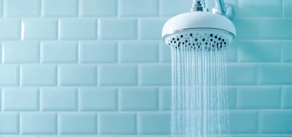 Duschkopf mit fließendem Wasser vor hellblauen Fliesen – Symbolbild für vergütungspflichtige Arbeitszeit