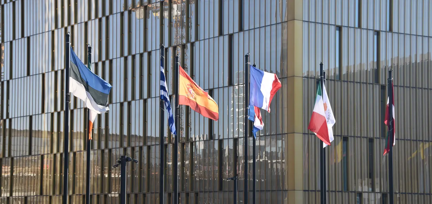 Mehrere nationale Flaggen wehen vor einer modernen Glasfassade.