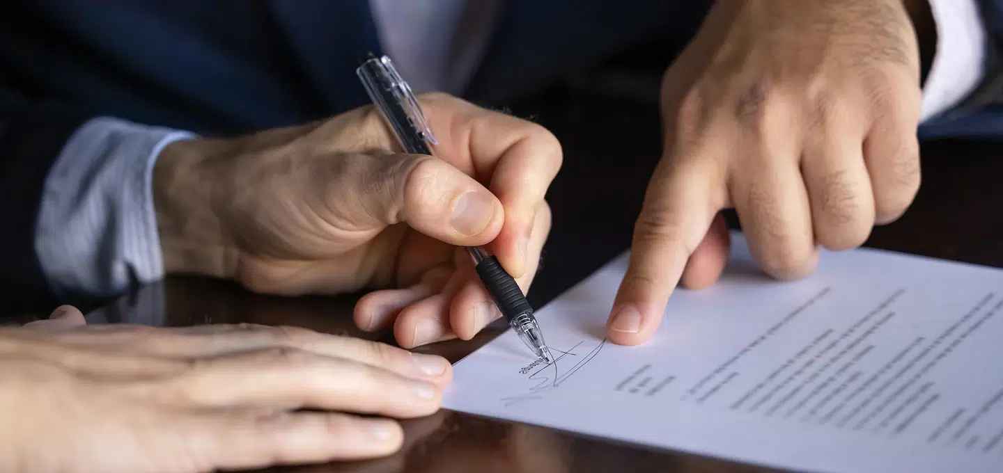 Symbolbild für Handelsvertretervertrag – Person unterschreibt Vertrag, während eine andere auf eine Vertragsklausel zeigt