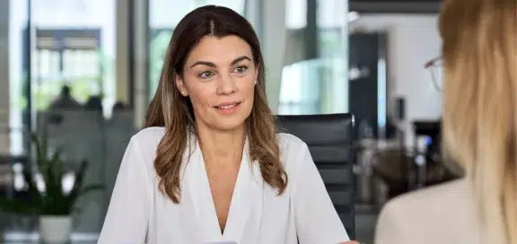A woman in business attire talking to a colleague in the office – discussing severance pay and the Pay Transparency Directive