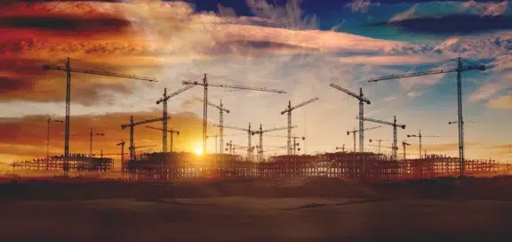 Baustelle mit mehreren Baukränen im Sonnenuntergang – Symbolbild zur Kündigungsvergütung im Bauvertragsrecht