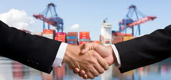 Handschlag zwischen Geschäftspartnern vor Containerhafen – Symbolbild für Zölle und Lieferverträge im internationalen Handel