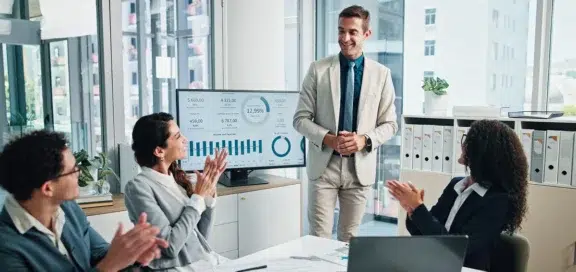 Zielvorgabe Schadensersatz: Team applaudiert Kollegen bei Präsentation von Unternehmenszielen im Meeting