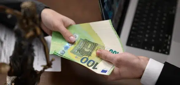 Hand übergibt Bündel 100-Euro-Scheine neben Justitia-Statue als Symbol für Vermögensabschöpfung bei organisierter Kriminalität