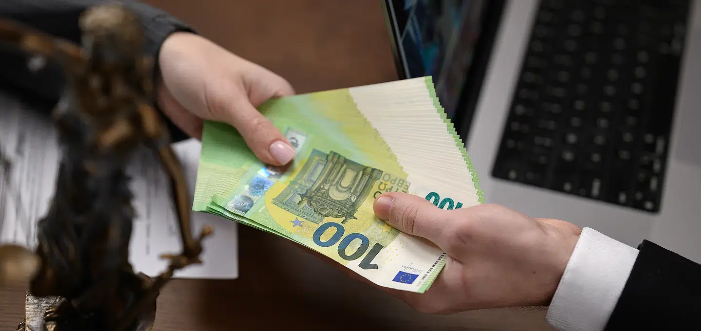 Hand übergibt Bündel 100-Euro-Scheine neben Justitia-Statue als Symbol für Vermögensabschöpfung bei organisierter Kriminalität