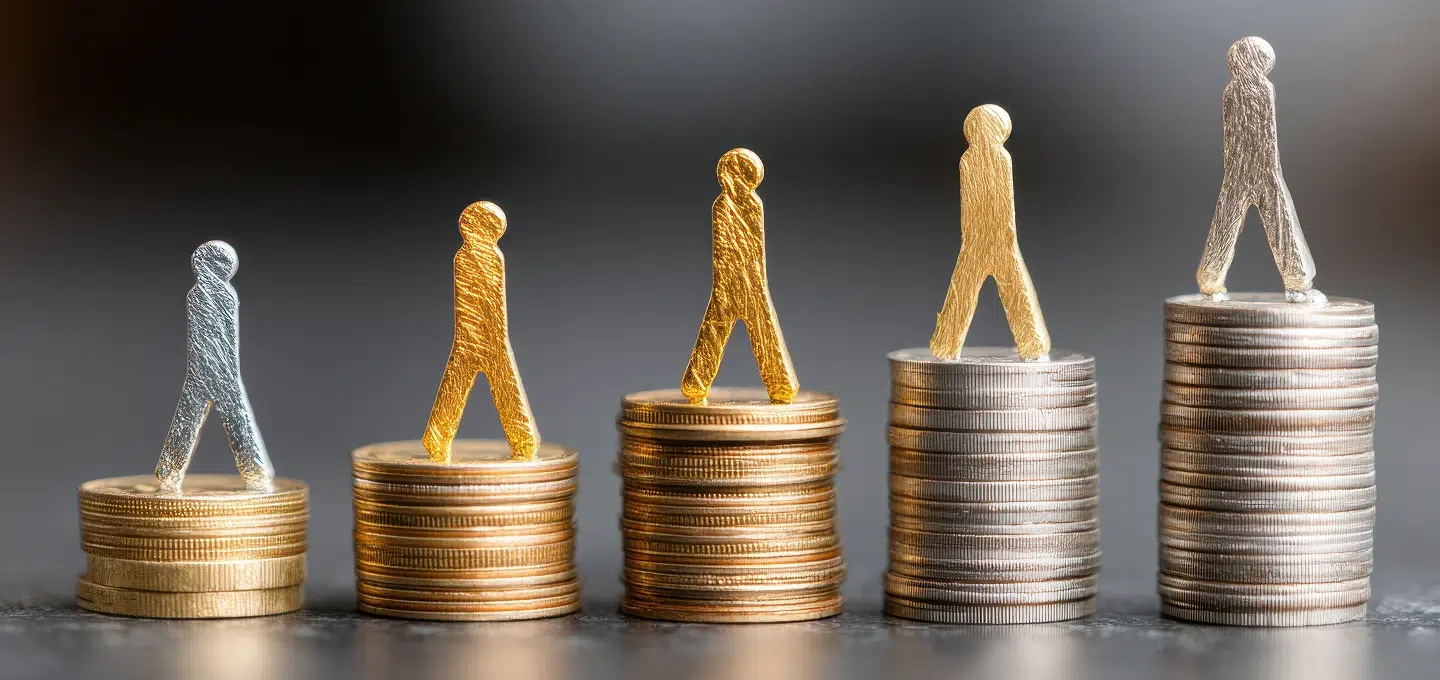 Fünf metallene Figuren unterschiedlicher Größe auf ansteigend hohen Münzstapeln als Symbol für Entgeltunterschiede und die Vorgaben der EU-Entgelttransparenzrichtlinie zu gleicher Bezahlung