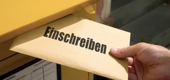 Brauner Briefumschlag mit Aufschrift „Einschreiben" wird in gelben Postbriefkasten eingeworfen – Symbolbild für den Anscheinsbeweis bei Einwurf-Einschreiben im Arbeitsrecht
