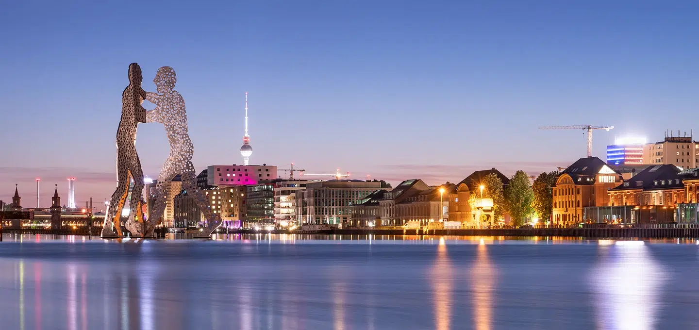 Skulptur „Molecule Man“ in der Spree vor der abendlichen Berliner Skyline mit Fernsehturm und Baukränen als Symbol für Zuzug und Wachstum durch Unternehmer nach § 21 AufenthG