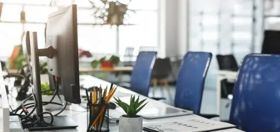 An empty, brightly lit office workspace with monitors, a pen holder, a succulent, and blue office chairs, symbolizing the time spent on legal proceedings during the wrongful termination case