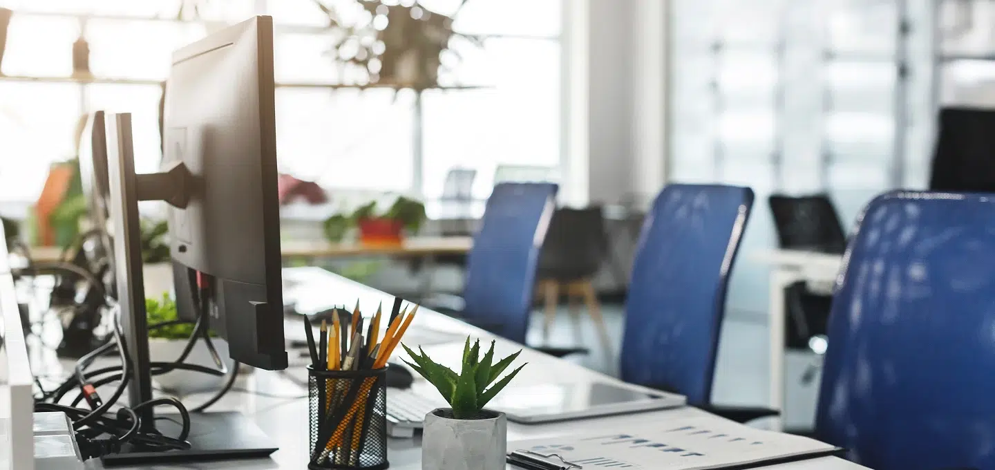 An empty, brightly lit office workspace with monitors, a pen holder, a succulent, and blue office chairs, symbolizing the time spent on legal proceedings during the wrongful termination case