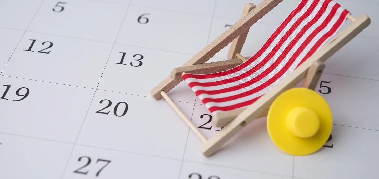 A miniature wooden deck chair with a red-and-white striped fabric cover and a yellow hat are placed on a monthly calendar with visible dates – symbolic for Urgent Court Orders for Leave